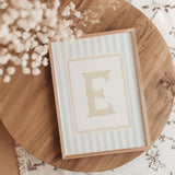 “A-Z alphabet initial nursery wall art printable set with pastel blue stripes and beige letters in wooden frames.”